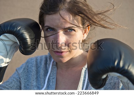 dynamic, natural and close up portrait of a young woman wearing boxing gloves her hair blowing in front of her face in the evening breeze