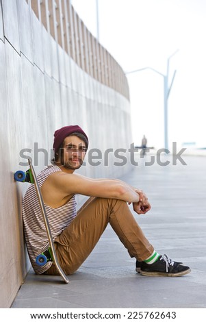 youthful streetwise man resting against a granite wall with a skateboard by his side