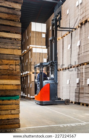 forklift lifting a pallet from the top shelf in a large warehouse