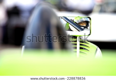 The nervous, tencely concentrated look in the eyes of a race car driver in his car on the starting grid of a race track, reflected in the side mirror of his vehicle.