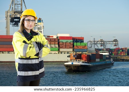 Female Shore Pilot looking into the camera whilst guiding an inland vessel to its mooring in a commercial harbor where a large container ship is being unloaded