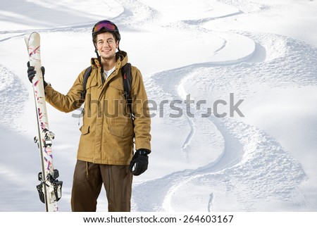 Young off piste skier standing in front of fresh tracks in the powder snow with skis in his hand