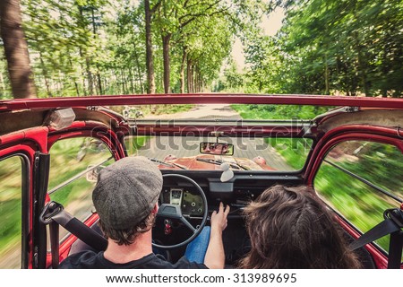 Couple in an ondtimer convertible, driving through the woods, carefree, enjoying the ride