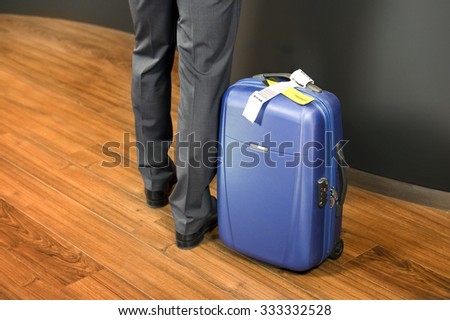 Business class passenger, with a carry on suitcase with priority luggage tags standing at an airport check-in counter