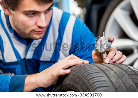 Mechanic, checking a measurement gauge to check the depth of a tread on a car tire for wear, to make sure it is still within regulations and safe to use. Focus on the hands and the gauge