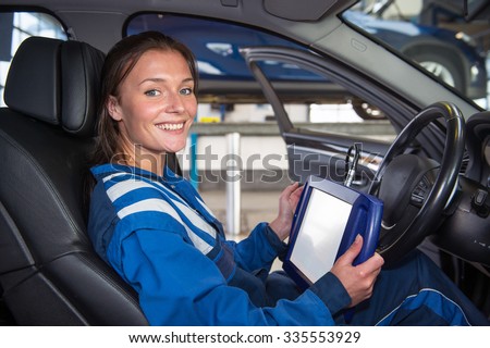 Female mechanic, running a diagnostics program, connected to the computer of the cars, sitting in the drivers seat using a sturdy touch screen terminal