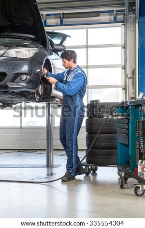 Mechanic, using a calipher, to check the thickness of a brake disk of a vehicle on a car lift. A stack of tires and a tools trolley behind him