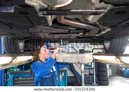 Fremale mechanic chaning the oil of a vehicle on a car lift, using a torque wrench to unscrew the oil tank. A collection vessel is placed underneath the outlet for environmental and recycling purposes