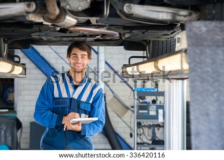 Portrait of happy male mechanic writing on clipboard under car in garage