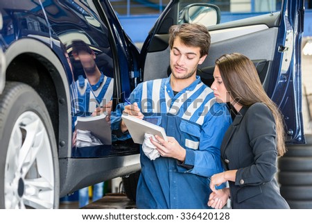 Car mechanic with female customer going through maintenance checklist in garage