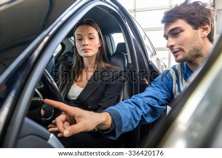 Young woman looking at mechanic checking light switch of car in garage