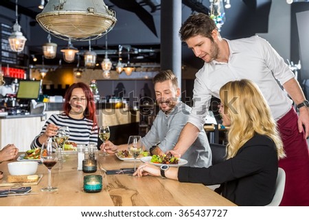 Young waiter serving food to customers at table in cafe