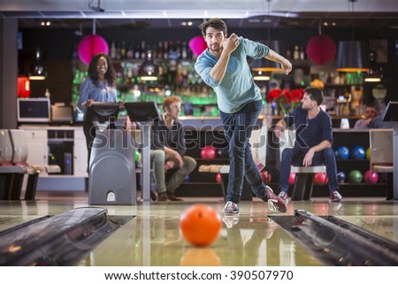 Group of friends are bowling and having fun, young man is throwing the ball at the bowling lane.
