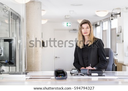 Sales woman, dressed in classy black, sitting behind the counter of a ticket booth in an office