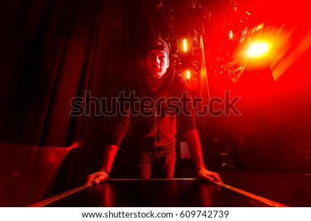 Roadie rolling a flightcase on stage, brightly lit by a red stage light.
