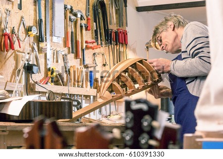 Luthier inspecting his halfway finished lute, standing behind his work bench, surrounded by the tools of the trade of a craftsman.