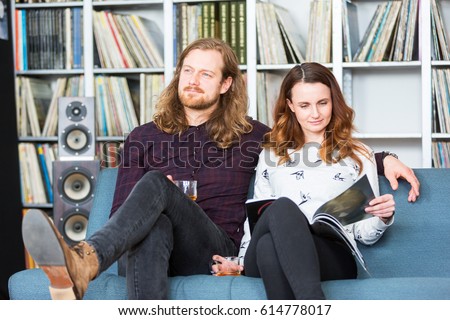 a couple relaxing toghether on a couch, reading and listening to music