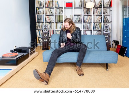 long haired man intensely ejoying rock music from vinyl  long playing record, on his sofa