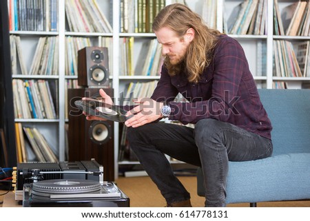 long haired man looking at the track list on a vinyl long playing record to put on the turntable