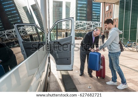 Taxi driver assisting male passenger with luggage by van at airport