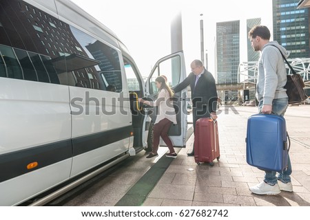 Taxi driver with luggage assisting female passenger to board van at airport