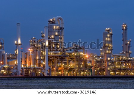 A petrochemical plant, with it\'s stainless steel cylinders, it\'s valves, chimneys, pipes, tubes and construction artificially lit just before the break of dawn