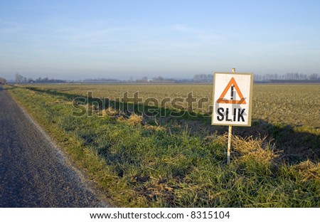 Low light, looking out over the plowed fields with a warning sign for slippery mud