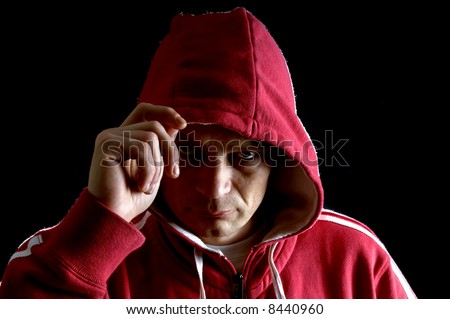 A grim looking hooligan, lifting his hood with his right arm, glaring at the camera.