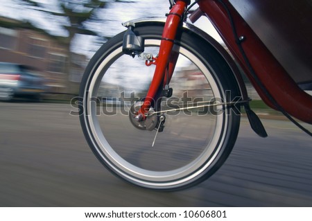 The spinning and vibrating wheel of a delivery bicycle on a suburban street