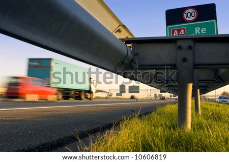A motorway safety rail with route information sign and motion blurred passing cars