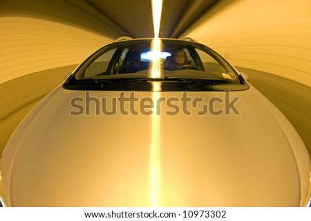 A car driving through a tunnel, seen from the hood, with the driver behind the wheel. A long exposure