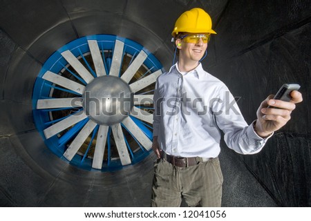 A smiling engineer, looking at his phone inside the realms of an industrial wind tunnel