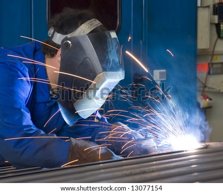 A welder, wearing a protective helmet and fire retardant clothing, working on steel beams