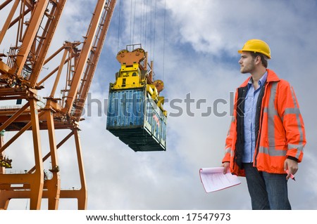 A Customs Control officer, checking the unloading of freight containers at an industrial harbor, wearing a hard hat and safety coat