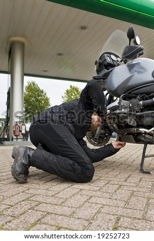 A motorist, checking the oil level of his motorcycle at a gas station