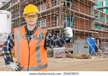 A satisfied looking construction worker giving a thumbs-up in front of a huge residential building site