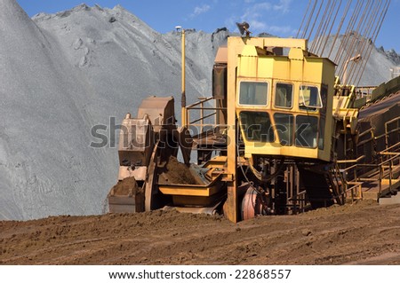 A wheel digger used to excavate minerals at a mine in front of a huge heap of iron ore in action