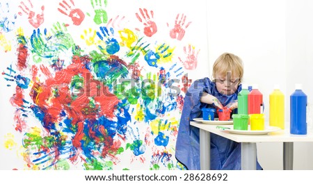 A young boy putting his hands in a pot with finger paint to get more red for his painting