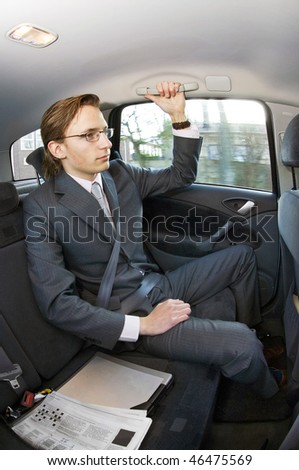 A businessman riding in the backseat of a taxi with laptop and newspaper next to him