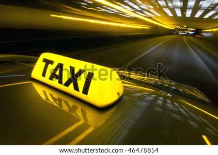 A cab at high speed on a motorway in an urban area with the lit taxi sign on top of its roof