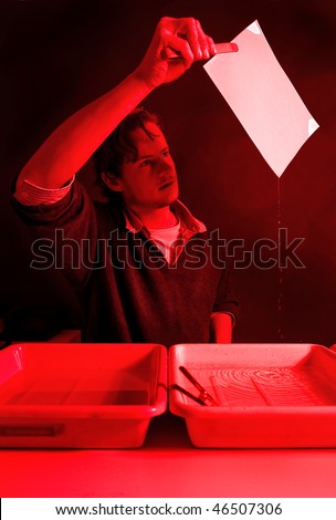 Photographer examining a fresh, still wet, print, directly from the stop bath in a dark room