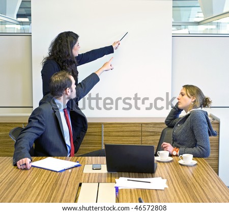 Two colleagues pointing at a presentation screen, trying to convince a bored looking businesswoman