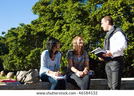 Three students talking on a small wall in a university park on a beautiful sunny day