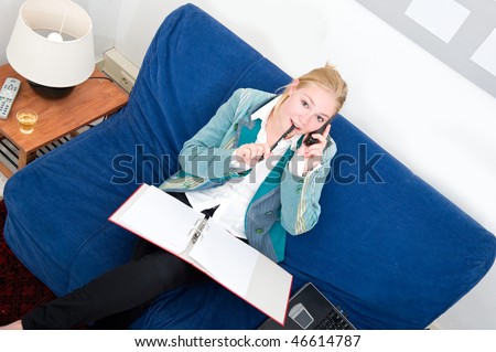 Business woman making a call with a dossier on her lap at home, sitting on a couch with laptop and a glass of white wine next to her