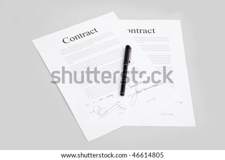 Pair of contracts containing generic text and fictitious signatures with a pen on the gray surface of a desk