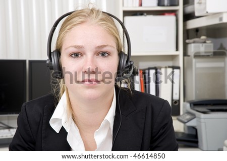 A woman wearing a head set with microphone as receptionist for a small business. An office setting in the background