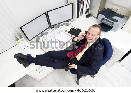 The owner of a small business relaxing behind his desk making several phone calls