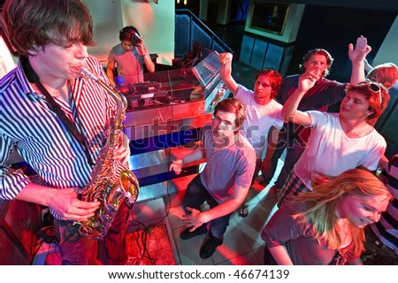 Party crowd going wild during a solo of a saxophonist, accompanied by a DJ