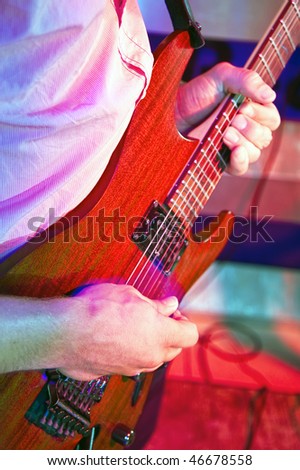 Looking over the shoulder of a guitarist at his hands, on a stage in a discotheque