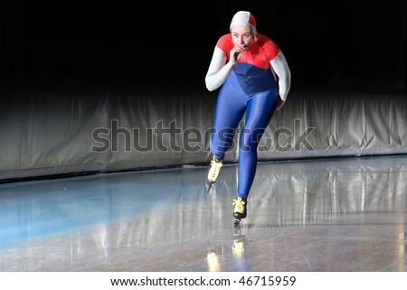 Speed skater emerging on the straight stretch of an indoor ice rink during a long distance skating race